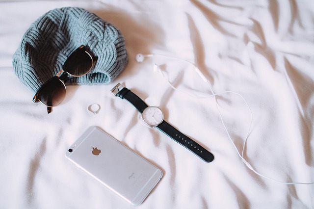 Iphone, hodinky, slúchadlá, čiapka a okuliare položené na bielej posteli.jpg